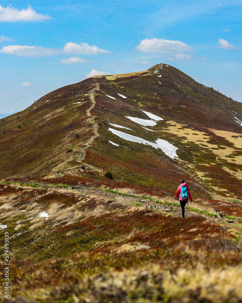 Fototapeta premium Beautiful fit happy girl in pink jacket enjoys hike in stunning colorful mountain scenery. Spring in the Bieszczady Mountains, Poland, Europe