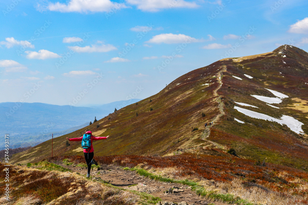 hiker girl stands on a mountain glade during spring; the girl spreads her arms enjoying the freedom and admiring nature awakening to life