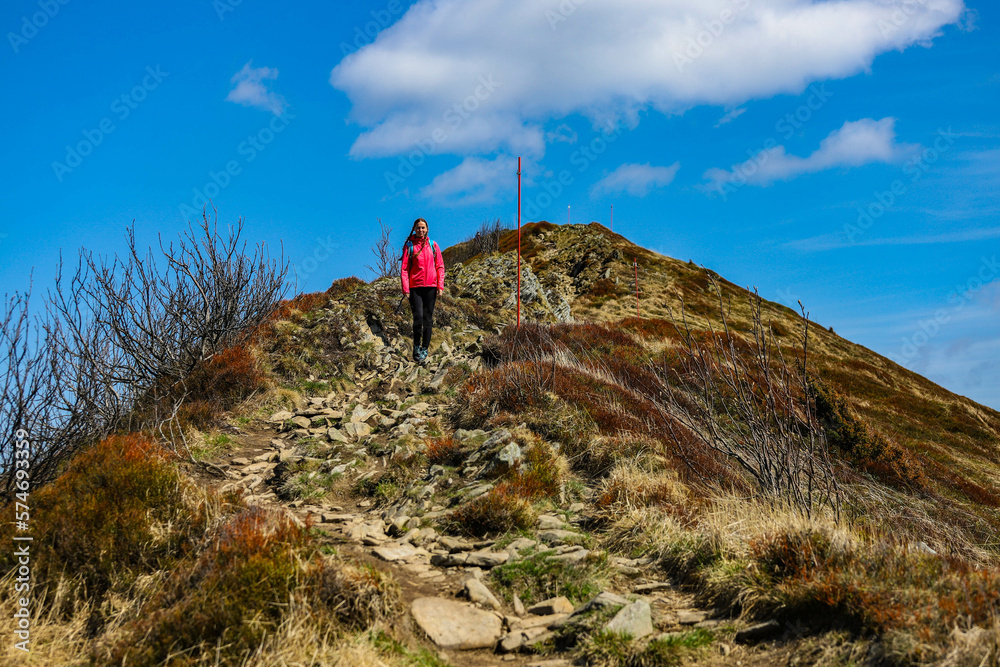 Beautiful fit happy girl in pink jacket enjoys hike in stunning colorful mountain scenery. Spring in the Bieszczady Mountains, Poland, Europe