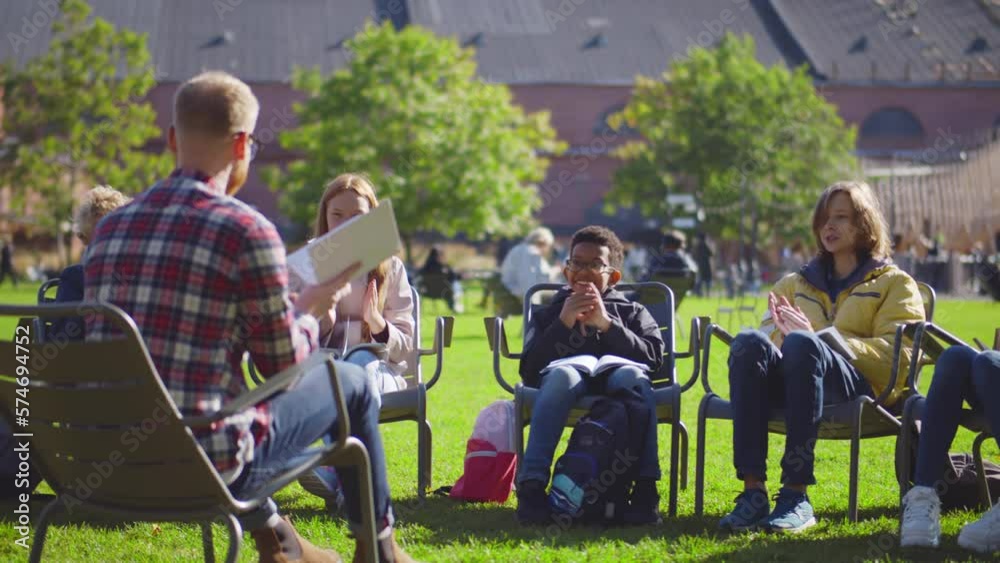 Group of high school students sit on lawn having outdoors lesson. Realtime Group of high school students sit on lawn having outdoors lesson. Realtime