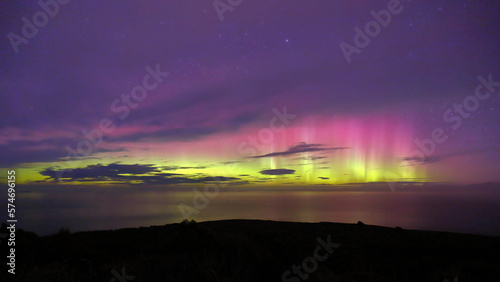 Aurora Australis or southern lights in Invercargill, New Zealand; beautiful purple, pink and green lights, with colourful clouds, ocean, night sky and mountains in the background