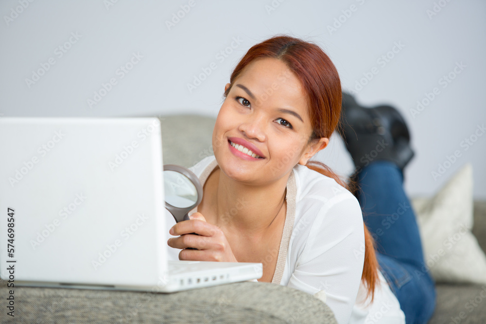 beautiful woman looking through the magnifying glass at her laptop beautiful woman looking through the magnifying glass at her laptop