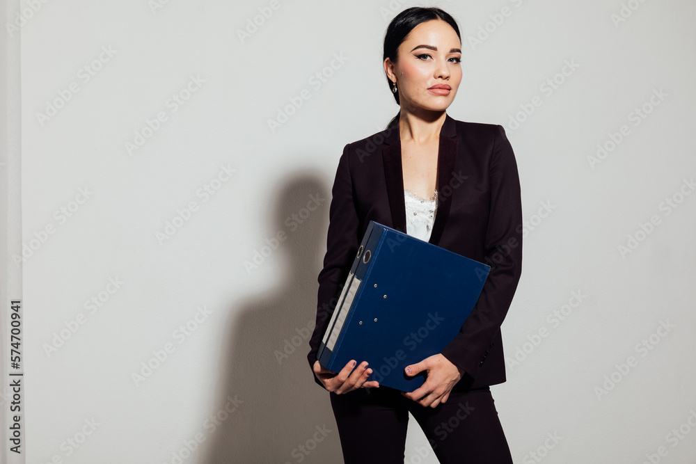 a business woman in a black suit stands with a folder in an office space