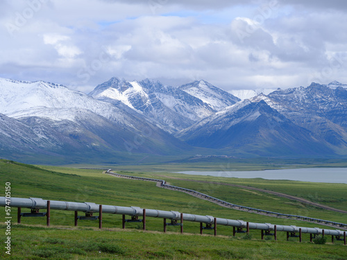 Fresh July snowfall on the mountains of the Brooks Range with the Alaska Oil Pipeline in the foreground traversing miles of empty Tundra