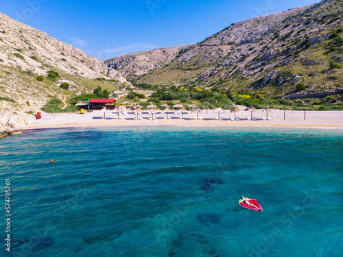 beautiful girl in bikini swims on a strawberry-shaped mattress in turquoise water in oprna bay on krk island, croatia; holiday on paradise beach in croatia