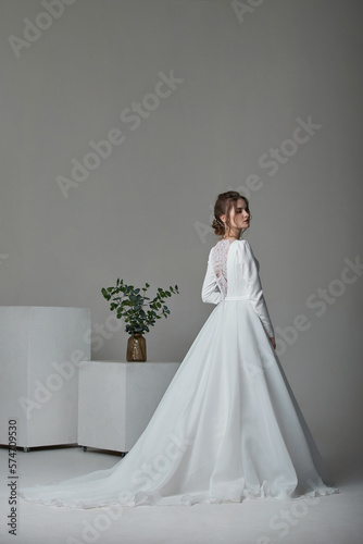 A beautiful young bride model in long lace dress in minimalist white studio interior. Wedding photography.