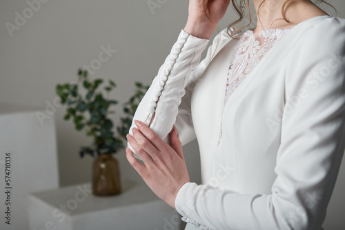 A beautiful young bride model in long lace dress in minimalist white studio interior. Wedding photography.