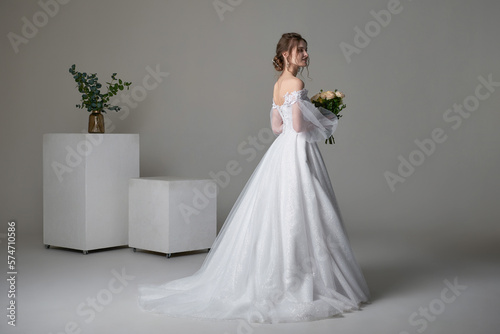 A beautiful young bride model in long lace dress in minimalist white studio interior. Wedding photography.