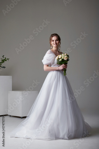 A beautiful young bride model in long lace dress in minimalist white studio interior. Wedding photography.