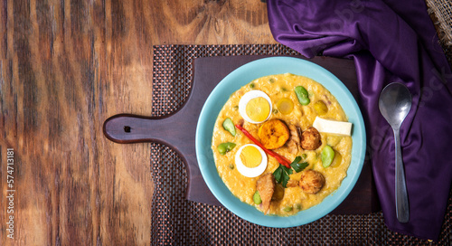 Top view of a turquoise fanesca dish with cod, hard-boiled egg and cheese on a wooden background and a purple napkin photo