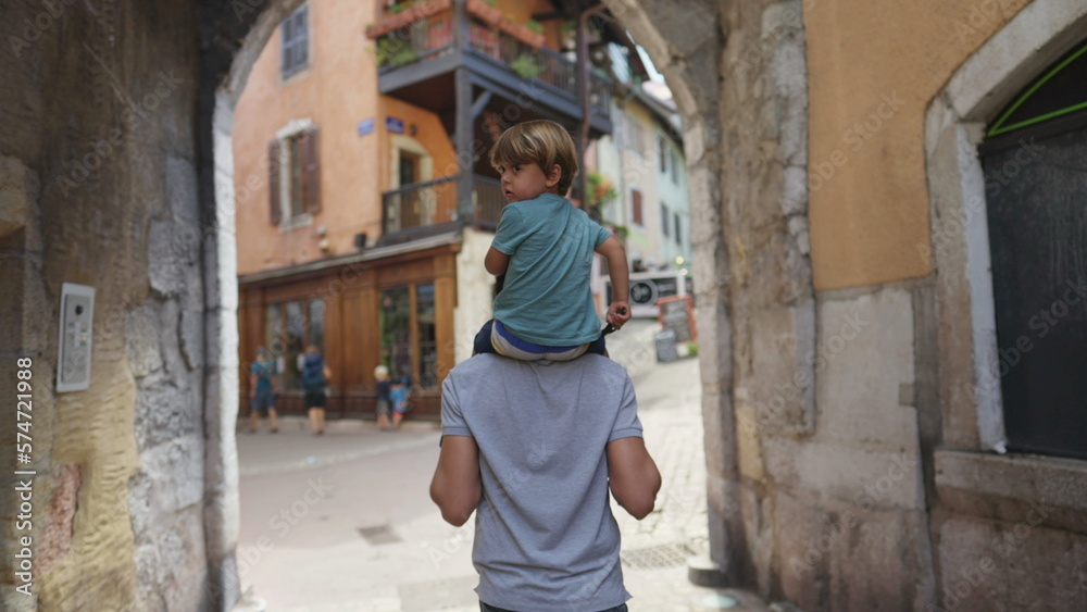 Back of child on father shoulders visiting traditional European city street. Family on vacations traveling to new place