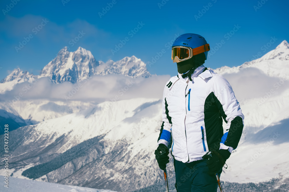 Portrait skier at ski resort standing on sunny day against backdrop of beautiful mountain peaks in the clouds