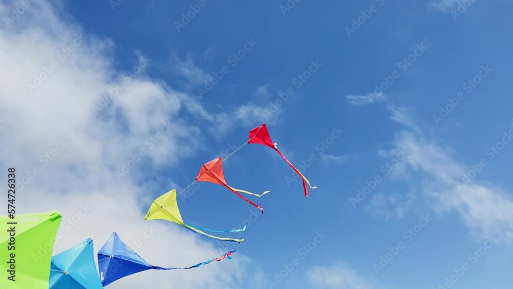 Many beautiful colorful kites fly over blue sky and clouds