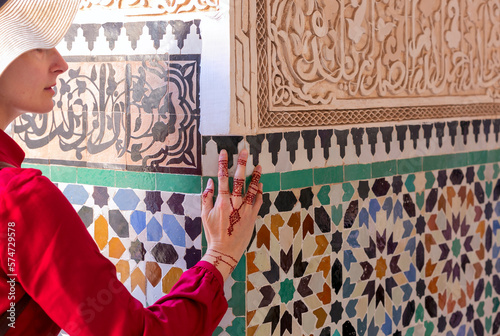Woman in red  dress touching  ceramic wall with floral pattern by hand in henna painting in marrakesc, marocco