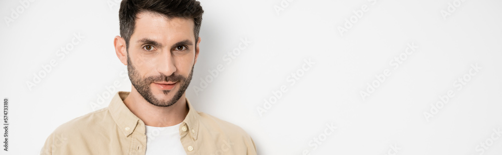 Obraz premium Brunette and bearded man looking at camera on white background, banner.