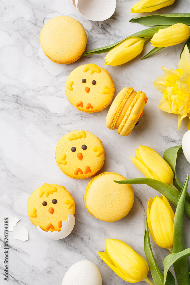Set of easter macaroon chicks with yellow tulips, daffodils and eggs over marble background. Top view, flat lay. Easter treat, holiday symbol