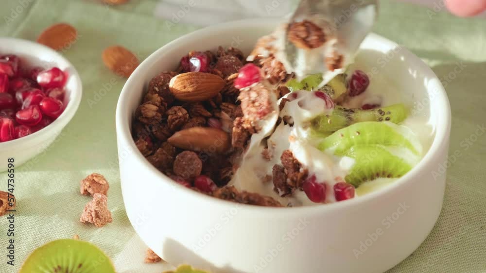 Man eating chocolate oat granola with yogurt, fresh kiwi fruit, pomegranate seeds, nuts with a spoon. Close up. Healthy breakfast. Tasty food Man eating chocolate oat granola with yogurt, fresh kiwi fruit, pomegranate seeds, nuts with a spoon. Close up. Healthy breakfast. Tasty food