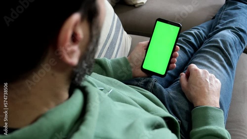 Man sitting on sofa makes single finger tap on smartphone green screen.