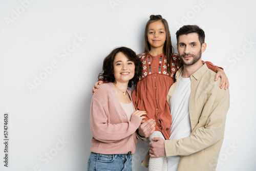 Smiling kid hugging parents and looking at camera on white background.