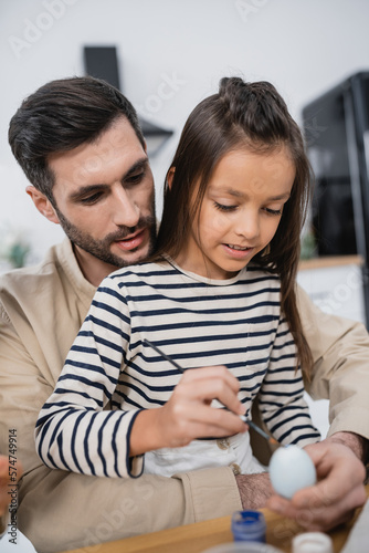 Child coloring Easer egg near bearded father in kitchen.