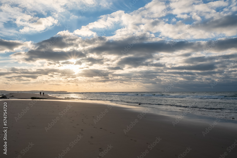 Sandy beach at the sea under a sky painted with clouds and a golden sun, showing an Amazing colorful sunset. Picturesque nature scenery.Clouds reflected in water. Zen-like tranquil atmosphere no