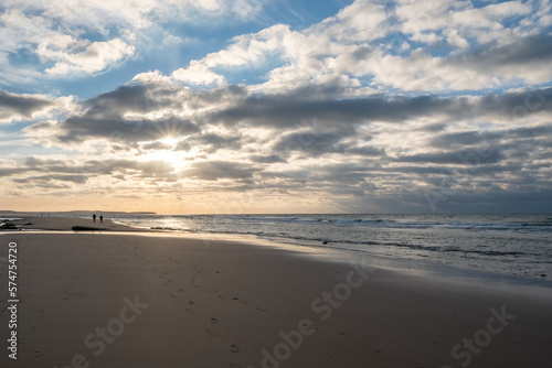 Sandy beach at the sea under a sky painted with clouds and a golden sun, showing an Amazing colorful sunset. Picturesque nature scenery.Clouds reflected in water. Zen-like tranquil atmosphere no