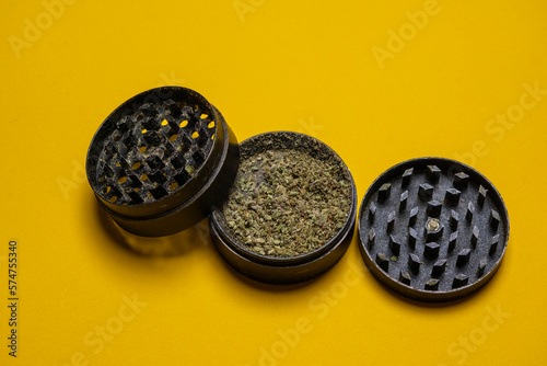Close up of high quality marijuana bud chopped inside a grinder on a yellow background.