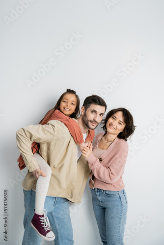 Cheerful girl piggyback on dad near mom on white background.