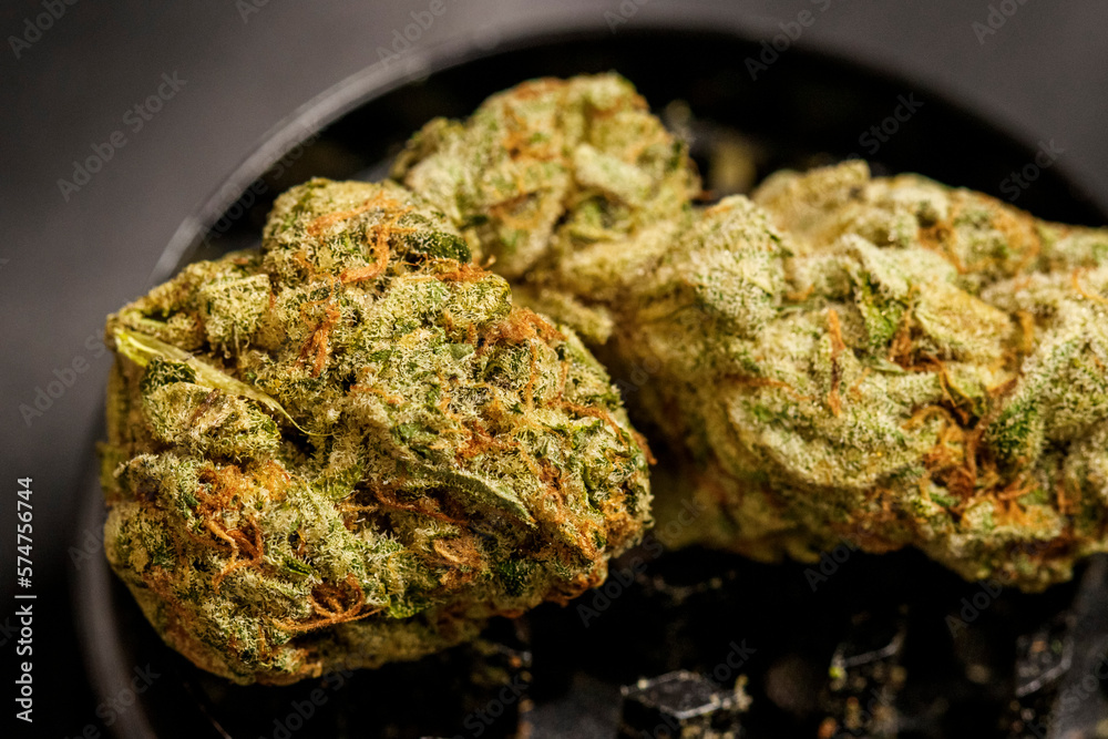 Close up of high quality marijuana bud with trichomes and crushed weed for chopping cannabis on a black table detail