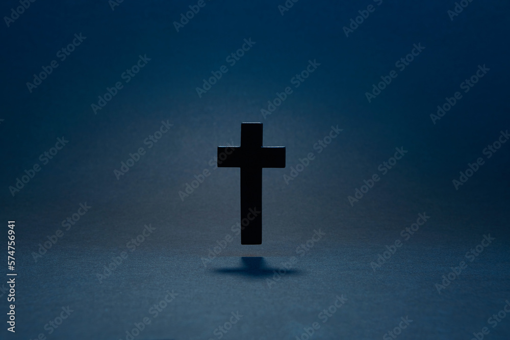 Black classic catholic cross hovering above the surface isolated on the dark solid fond blue background