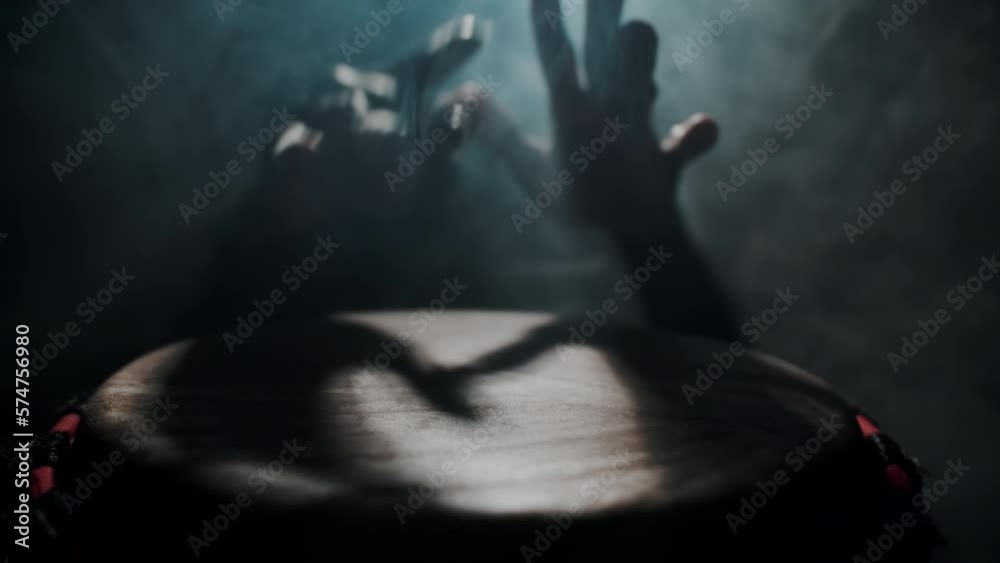 Close-up of the hands of a shaman black man playing an African folk drum, against a background of smoke. A black man plays a bongo drum. The concept of folk ethnic music