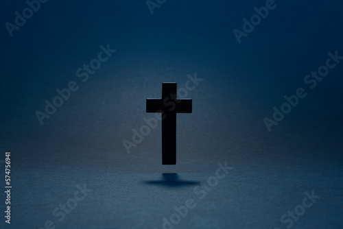 Black classic catholic cross hovering above the surface isolated on the dark solid fond blue background