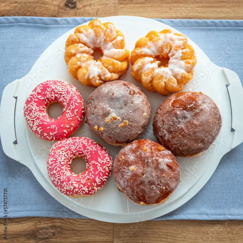A set of donuts on a plate, glazed with frosting with pink icing and sprinkles.