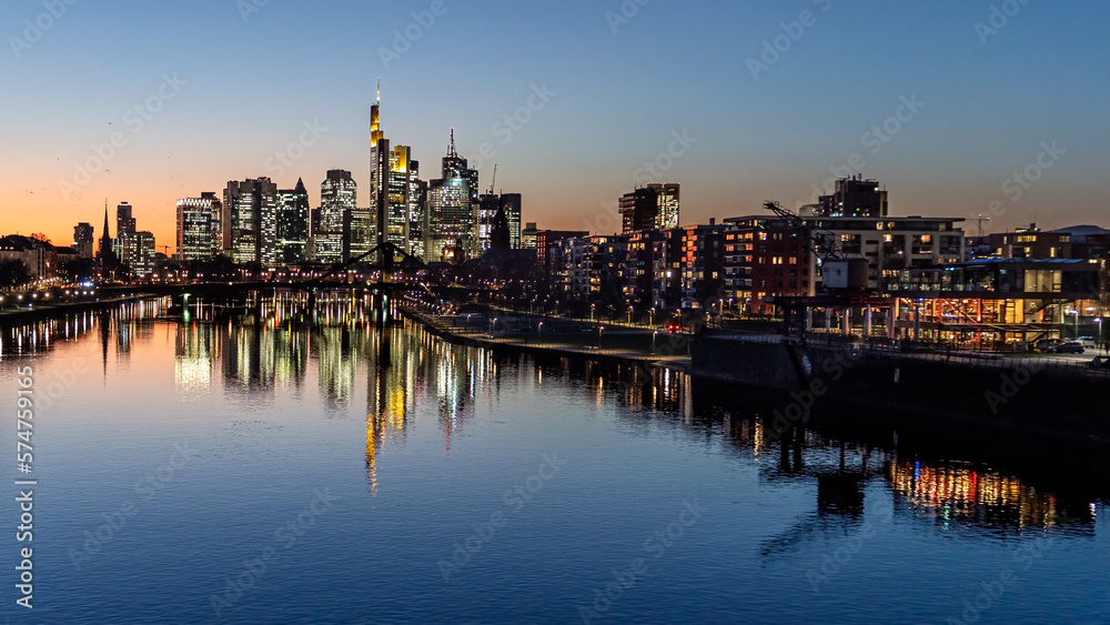 Illuminated city skyline in the evening under the clear sky with the river in the foreground