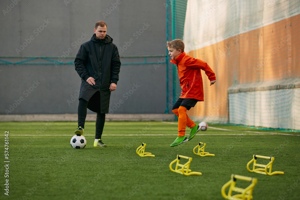 Boy, child, football player doing exercises, warming up before training session with coach on sports field outdoors. Concept of sport, childhood, active lifestyle, hobby, sport club