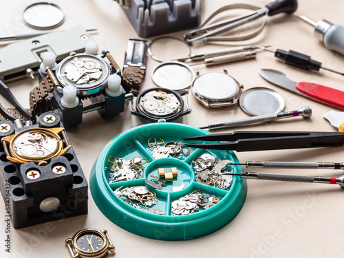 clock spare parts in tray, tools and open watches on wooden table in watchmaker workshop photo
