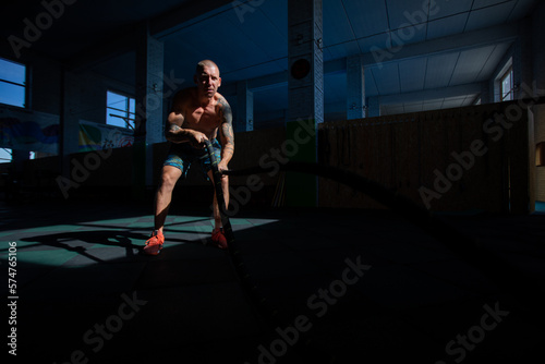 Athletic man doing double wave exercise with ropes in crossfit gym. © kanashkin