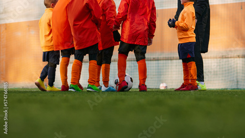 Cropped image of male legs on grass of sports field outdoors. Children playing football with coach. Concept of sport, childhood, active lifestyle, hobby, sport club