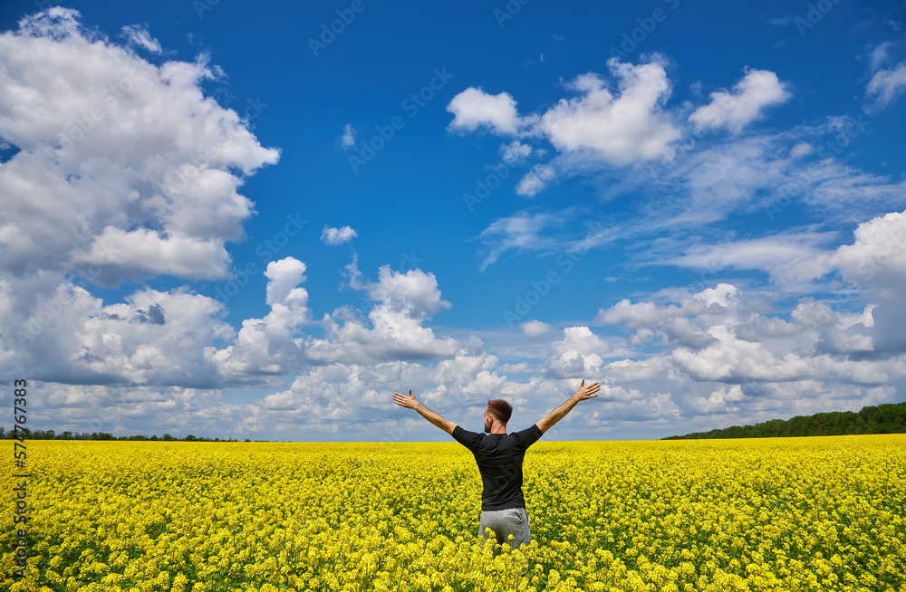 Man with arms outstretched. Handsome young man standing in a field of blooming yellow rapeseed flowers. Man with arms outstretched. Handsome young man standing in a field of blooming yellow rapeseed flowers.