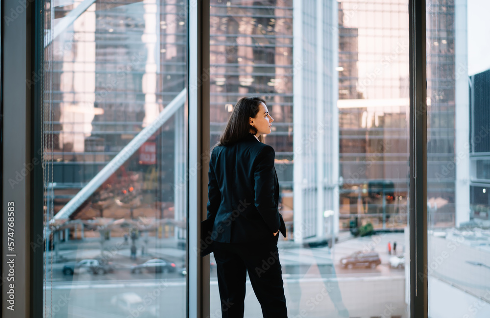 Young businesswoman standing against big window with hand in pocket Young businesswoman standing against big window with hand in pocket