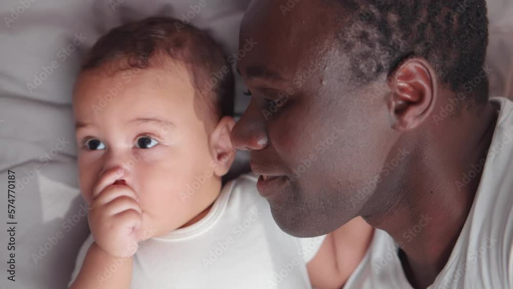 Adorable African American baby lying with father in bed. Realtime Adorable African American baby lying with father in bed. Realtime
