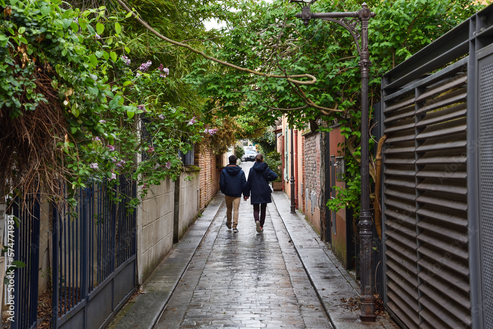 Couple Walking Hand in Hand along Green Cobblestone Alleyway in Paris, France