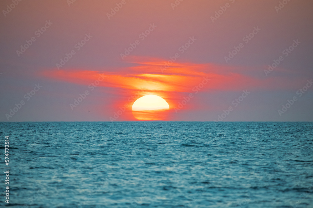 Sunset. Big sun on horizon. Red clouds on the sky. Beautiful seascape. Ocean beach or coast. Florida Gulf of Mexico. Good for travel agency. Spring or summer vacation. Orange sunlight. Tropical Nature