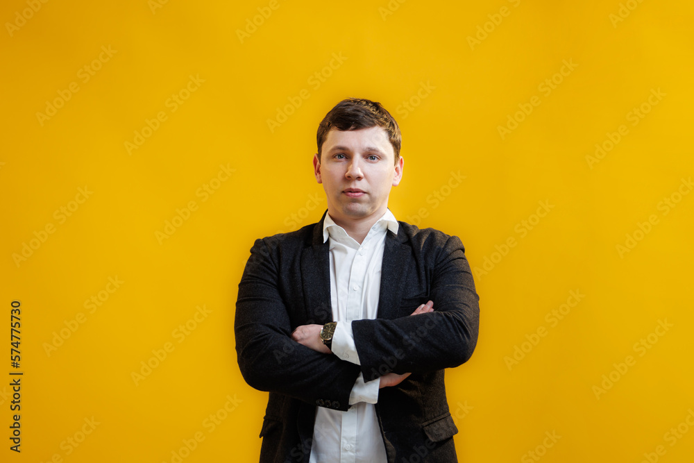 Portrait of handsome businessman with crossing hands standing on yellow studio background and looking at camera Portrait of handsome businessman with crossing hands standing on yellow studio background and looking at camera