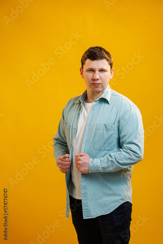 Portrait of handsome european man in shirt looking at camera standing on yellow studio background