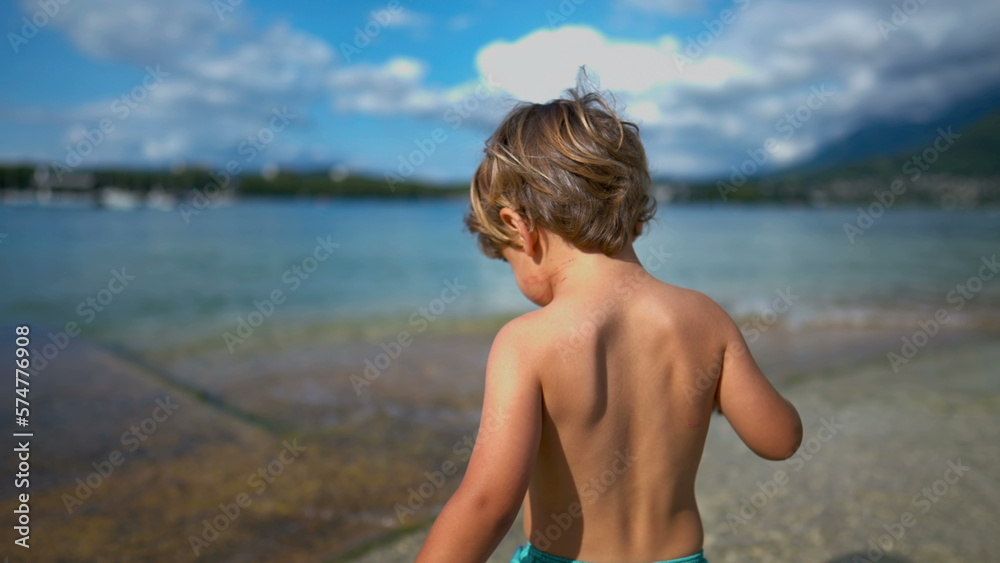 One small boy walks at beach shore during summer vacations. Child walking outdoors shirtless enjoying nature. Happiness concept One small boy walks at beach shore during summer vacations. Child walking outdoors shirtless enjoying nature. Happiness concept