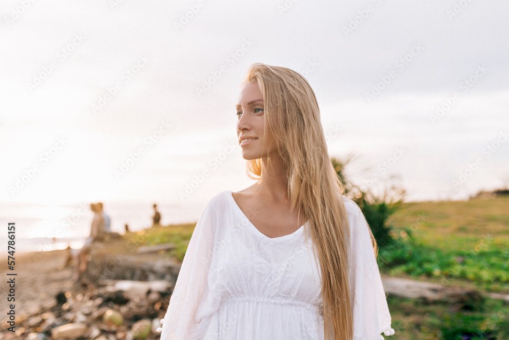 Elegant woman with long hair wearing white shirt with happy smile looking aside and enjoying ocean view in sunny warm day. Relax, vacation mood