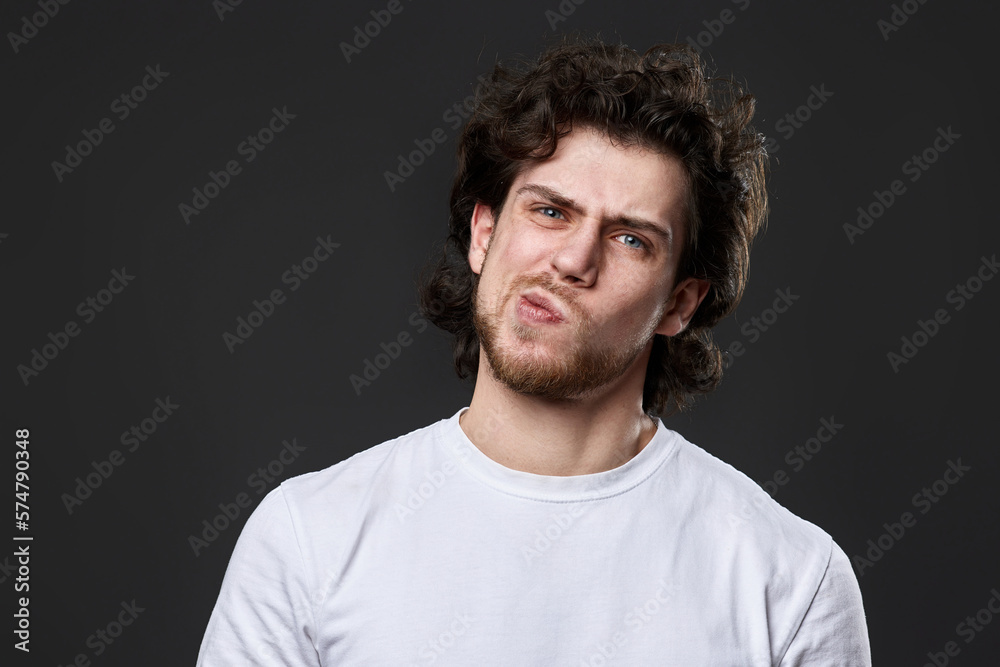 skeptic and nervous man in white t-shirt on dark gray background skeptic and nervous man in white t-shirt on dark gray background