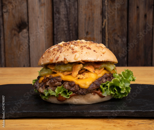 Multilayer hamburger. Closeup view of a cheddar cheese and guacamole burger in a black dish with a wooden background. 