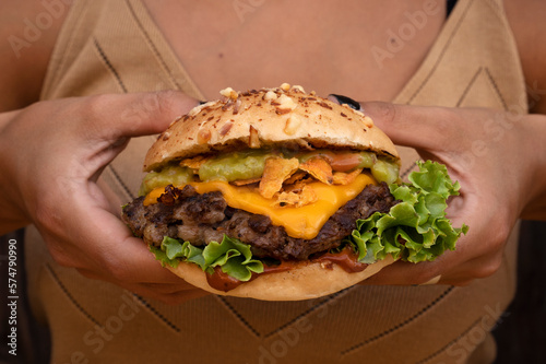Closeup view of a woman holding a giant gourmet burger with meat, guacamole, lettuce and cheddar cheese.